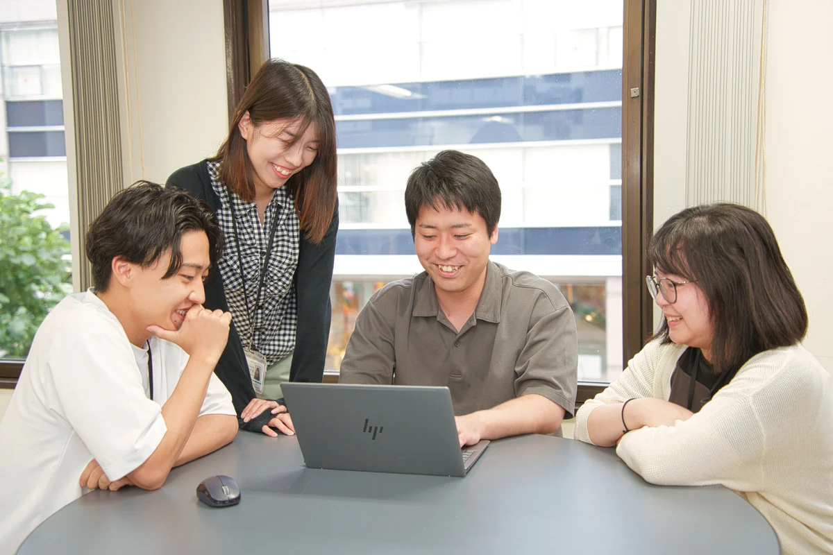 ノートパソコンを囲んで話し合う社員